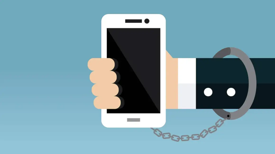 Eine Hand hält ein Smartphone, das mit einer Handschelle und Kette gefesselt ist. Ein Symbol für zu viel Handy-Nutzung.