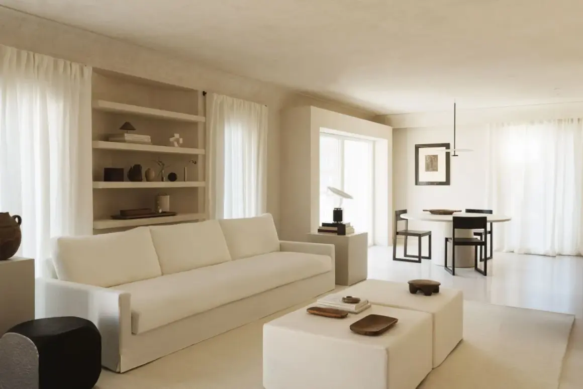 Minimalist Wohnzimmer mit weißem Sofa, Beistelltischen und Essbereich. Ein Beispiel für einen modernen Lebensstil, der Ruhe und Ordnung ausstrahlt.