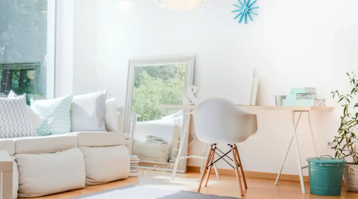 Ein helles, aufgeräumtes Wohnzimmer mit weißem Sofa, Spiegel und Schreibtisch. Perfekt, um das **Zimmer auszumisten** und Ordnung zu schaffen.