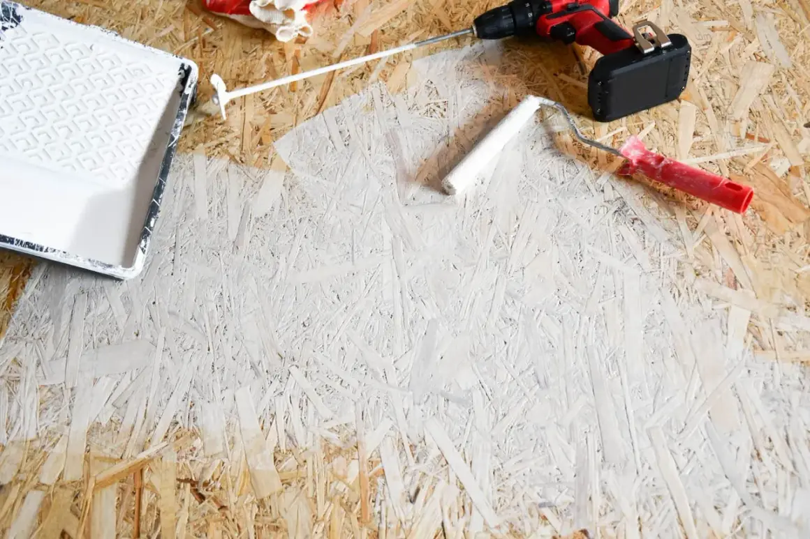 OSB-Platten streichen: Ein weißer Farbroller und eine Farbwanne liegen bereit. Ein Akkuschrauber und Handschuhe deuten auf ein DIY-Projekt hin.