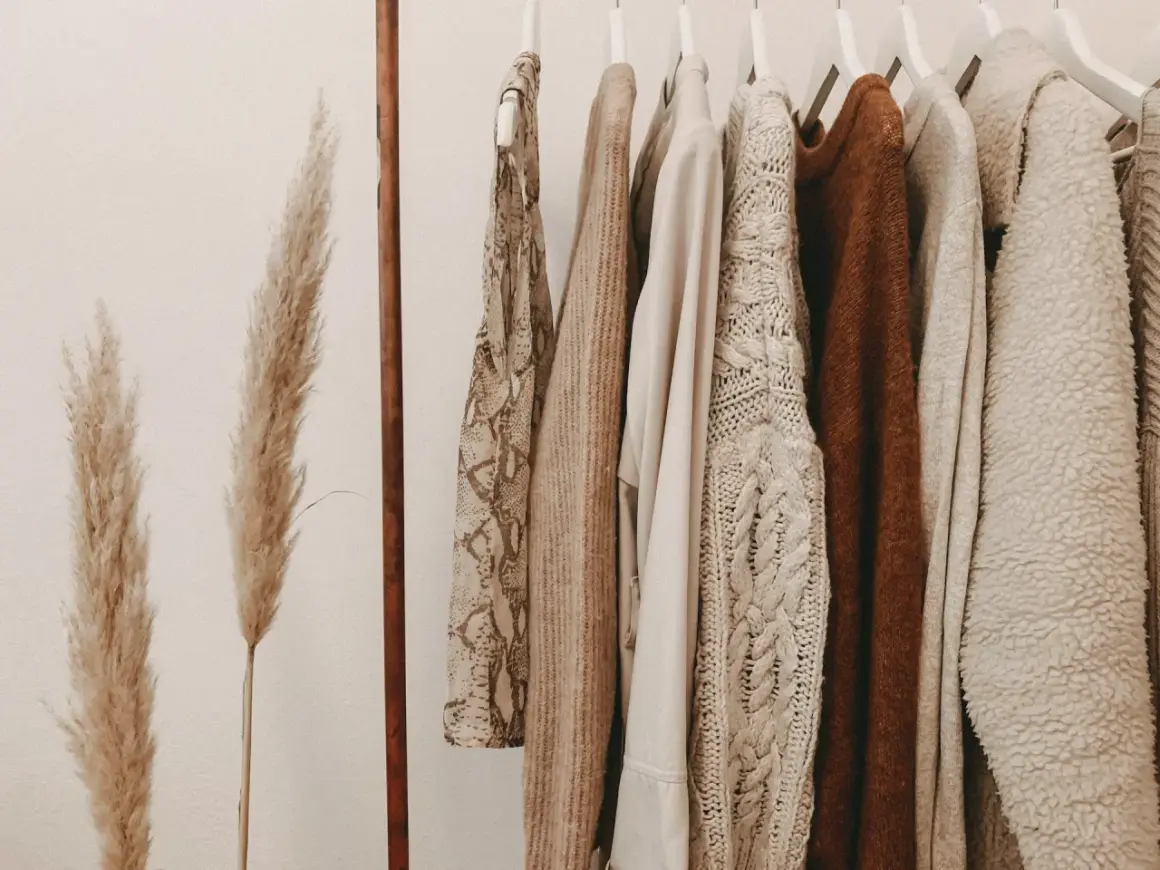 Kleidung in Erdtönen an einer Kleiderstange. Ein Statement gegen Fast Fashion: Qualität statt Quantität.
