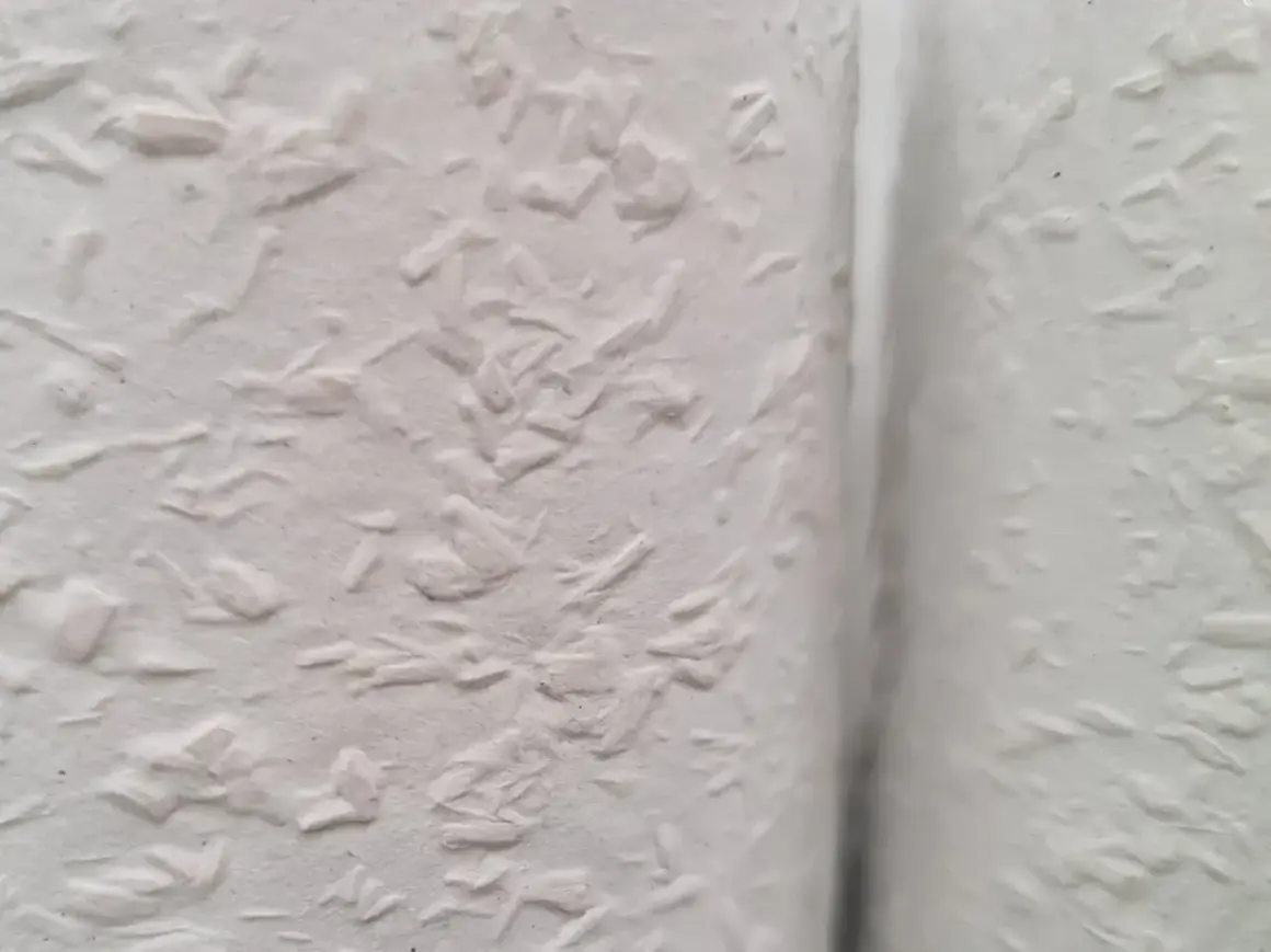 Nahaufnahme einer weißen Wand mit Raufaserputz innen. Die Struktur ist unregelmäßig und rustikal, perfekt für ein gemütliches Zuhause.