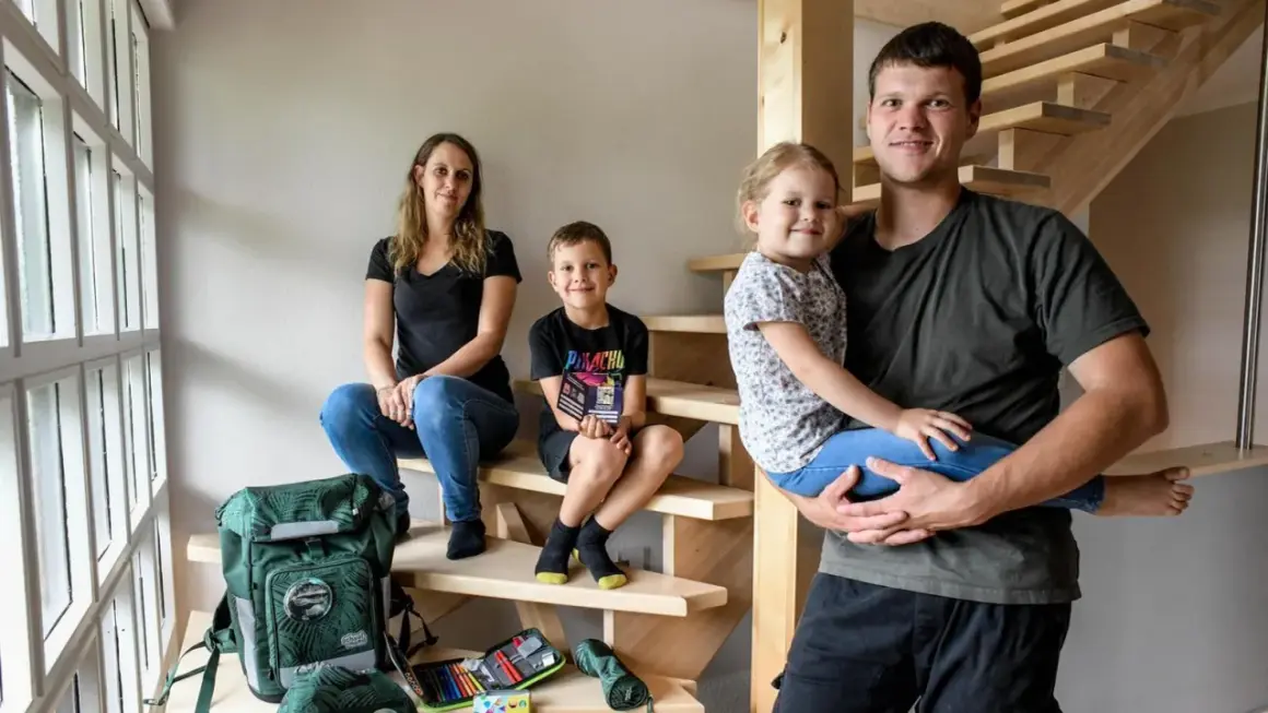 Familie auf Treppe, bereit für die Einschulung. Der Vater hält die Tochter, der Sohn sitzt daneben. Schulranzen und Mäppchen sind schon da.