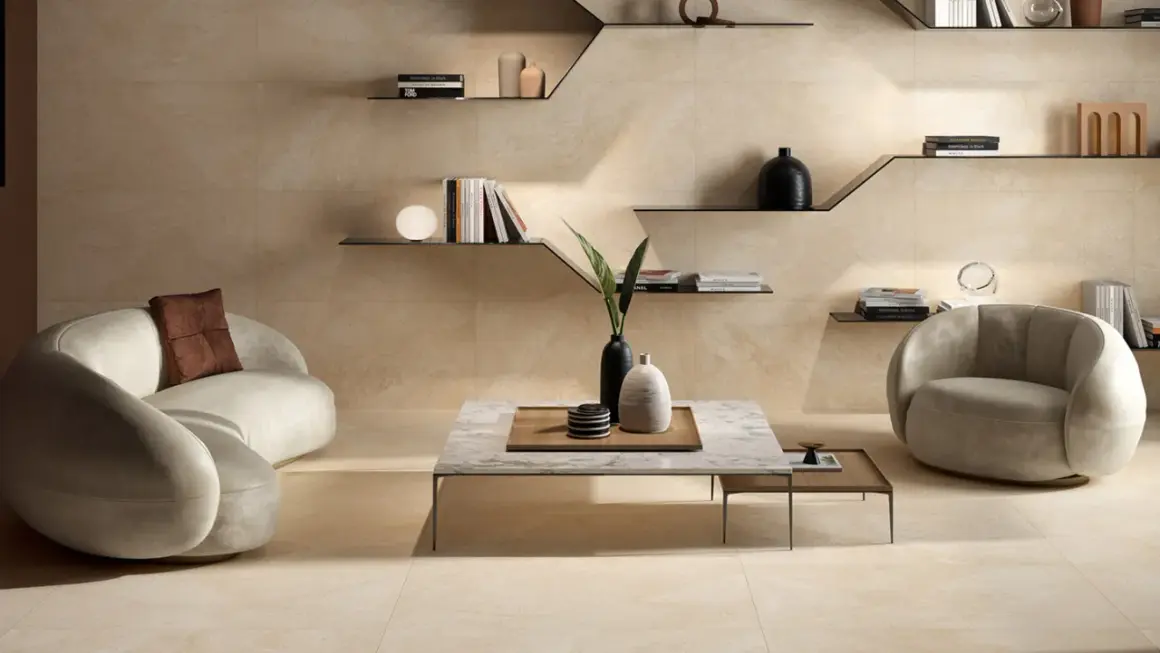 Ein Wohnzimmer in warmen Beigetönen. Ein geschwungenes Sofa und ein Sessel laden zum Entspannen ein. Die Wandfliesen zeigen, wie die Farbe Beige aussieht.