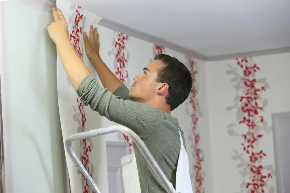 Mann bringt fototapete auf raufaser an. Rote Blumenmuster zieren die Wand.