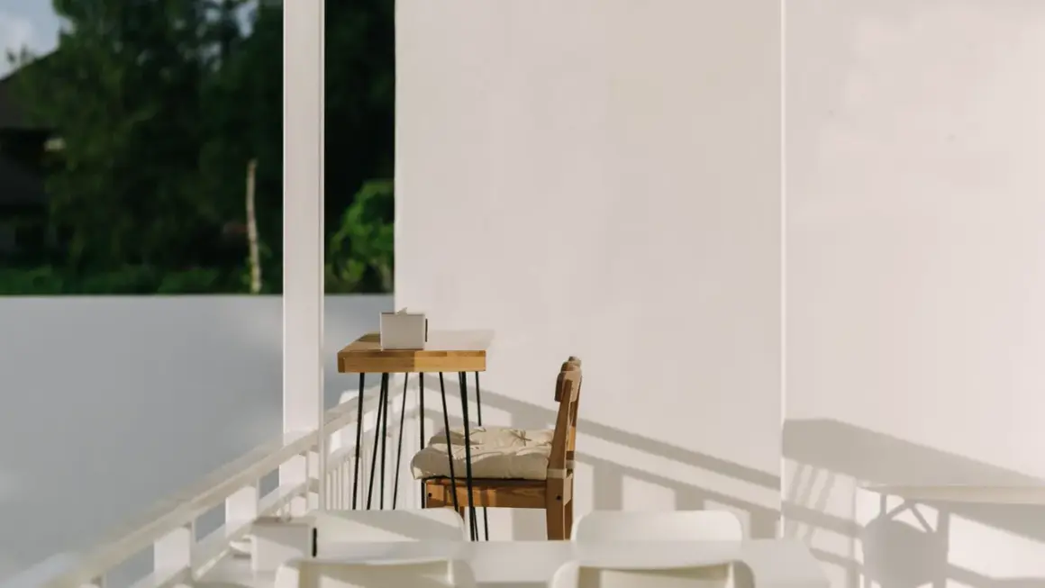 Ein Holztisch mit einer Box, ein Stuhl mit Kissen und weiße Möbel auf einer Terrasse. Hier lässt es sich schlicht und einfach leben.