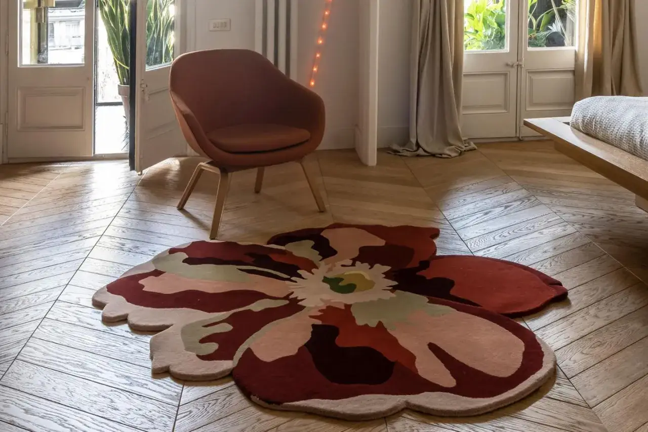 Blumenförmiger Teppich im modernen Design, ein echter Teppich Trend. Ein orangefarbener Sessel steht daneben.
