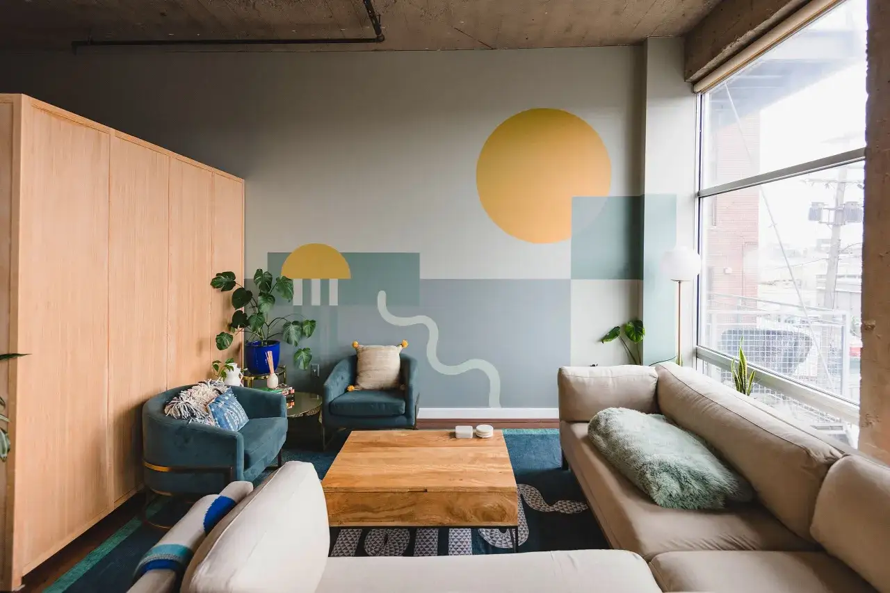 Modernes Wohnzimmer mit geometrischem Wanddesign streichen, zwei türkise Sessel, ein beiger Sofa und ein Holztisch.