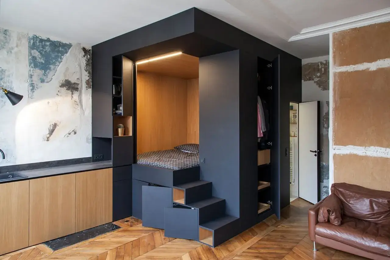 Cleveres Wohnzimmer: Ein gem&uuml;tliches Bett statt Sofa, integriert in eine schwarze Einbaul&ouml;sung mit Holzverkleidung und Stauraum.