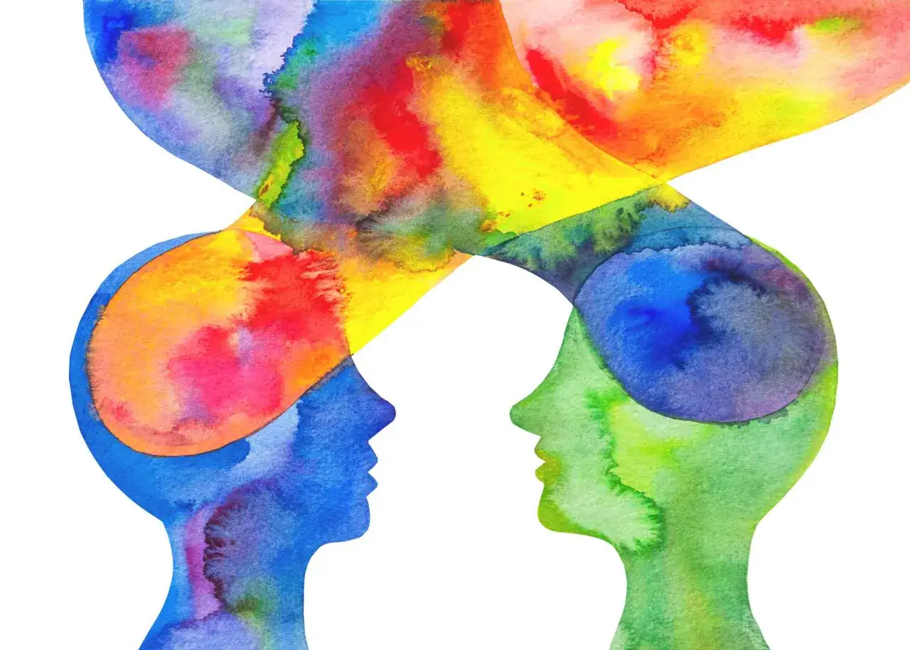 Zwei stilisierte K&ouml;pfe in Blau und Gr&uuml;n, die sich gegen&uuml;berstehen. Ihre Gedanken, dargestellt durch lebendige Farben, vermischen sich in der Mitte. Ein Symbol f&uuml;r die Vielfalt der Charaktereigenschaften und die Kraft der Farben.