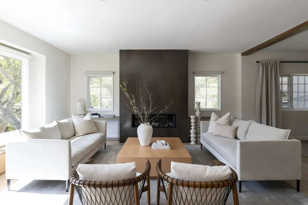 Ein helles Wohnzimmer mit zwei Sofas, einem Holztisch und einem Kamin. Die Einrichtung spiegelt minimalistisch leben erfahrungen wider: Weniger ist mehr.