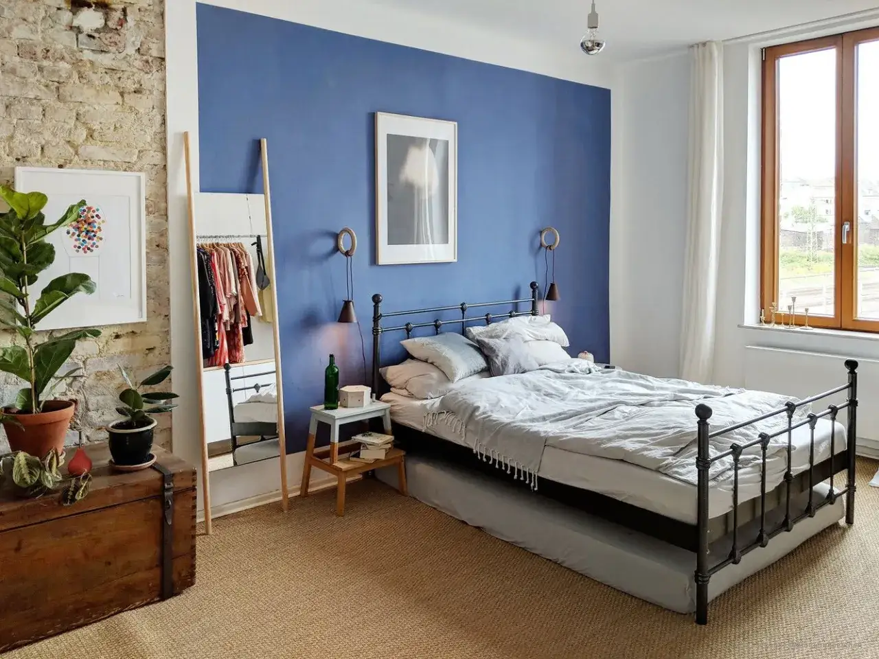 Ein Schlafzimmer mit einem blauen Bett und einer auff&auml;lligen blauen Wandfarbe. Ein Spiegel und Kleidung stehen neben dem Bett.