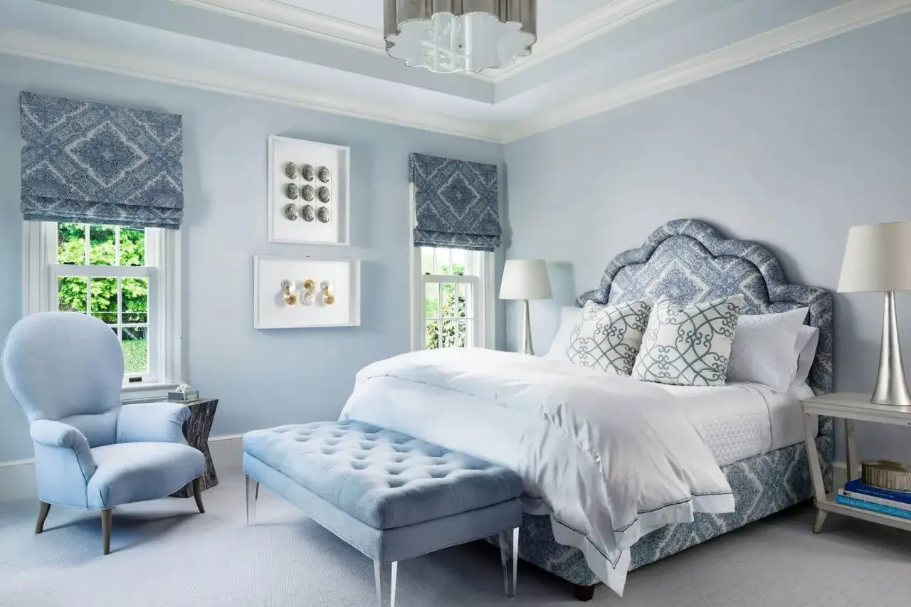 Ein stilvolles Schlafzimmer blau grau mit einem auffälligen Bettkopfteil, einem Sessel und einem Hocker.