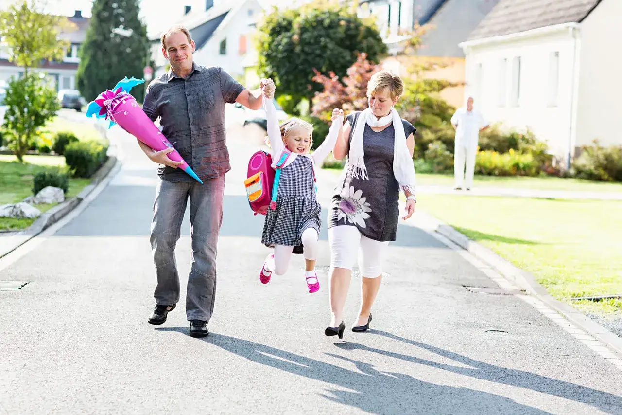 Familie geht zur Einschulung. Vater tr&auml;gt Zuckert&uuml;te, Mutter und Kind sind fr&ouml;hlich. Das Kind tr&auml;gt ein schickes Kleid, perfekt, was zur Einschulung anziehen.