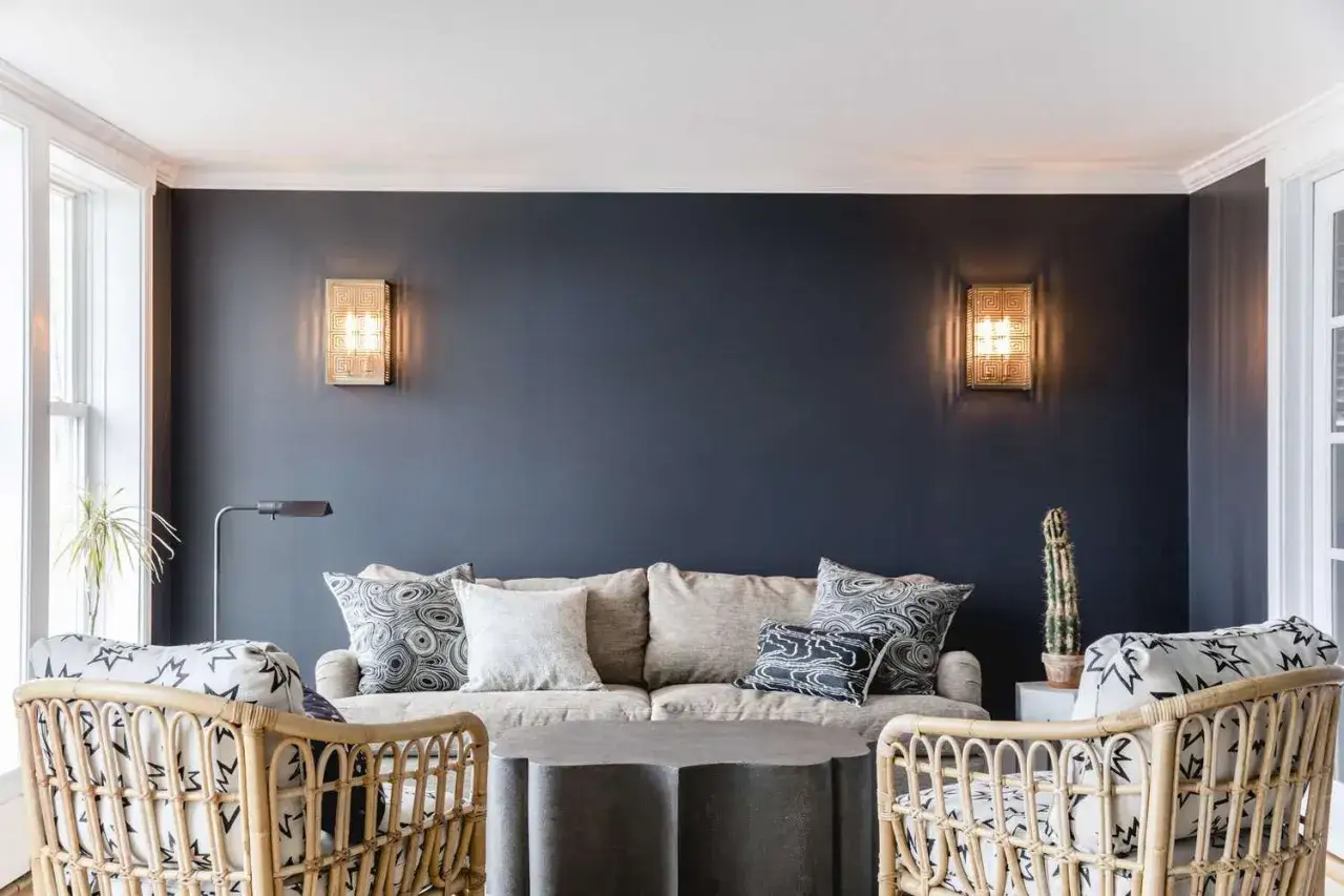 Ein gemütliches blaues Zimmer einrichten mit einem beigen Sofa, Korbstühlen und dekorativen Kissen. Wandleuchten spenden warmes Licht.
