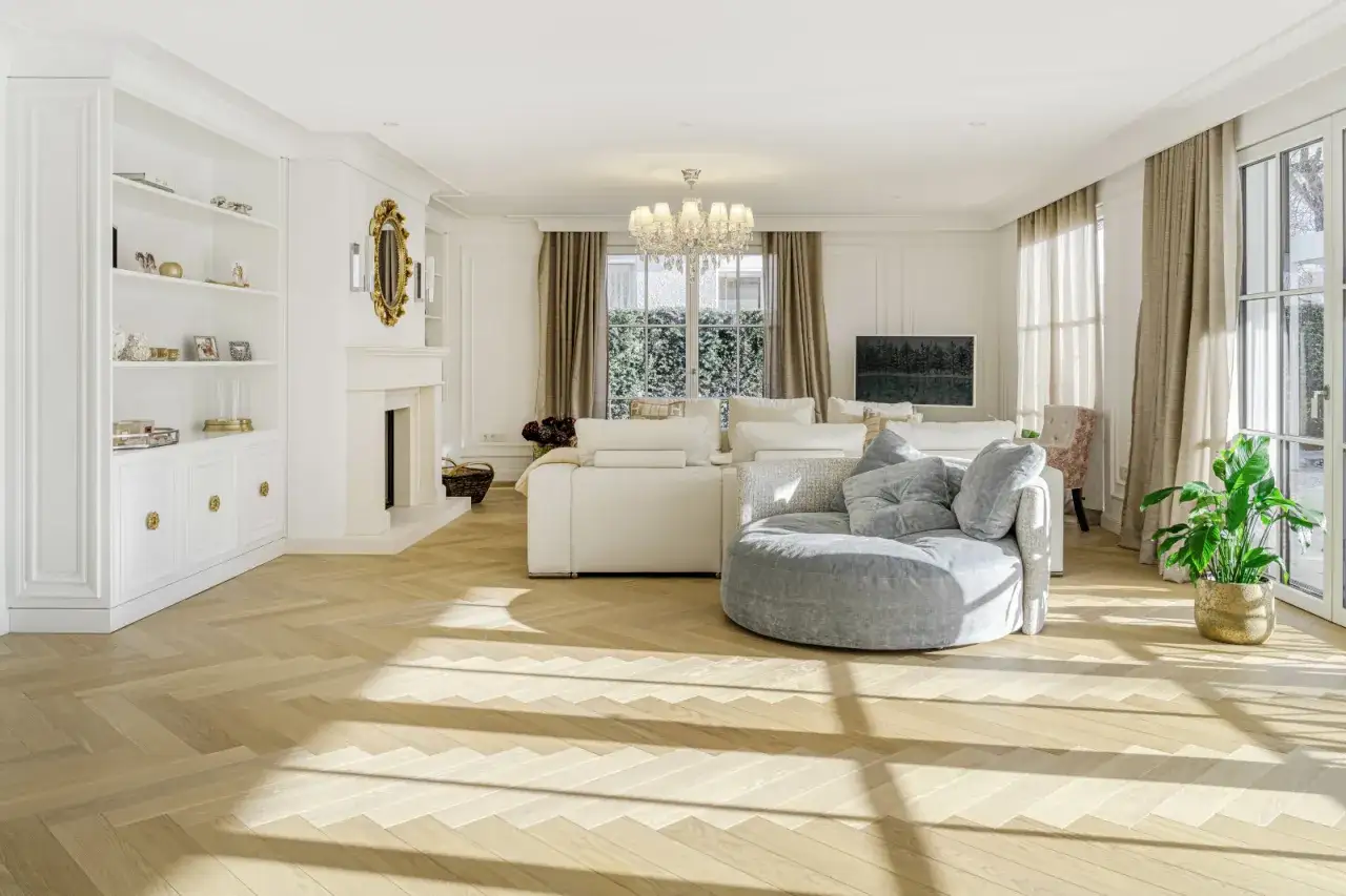 Heller Boden im Wohnzimmer mit Parkett im Fischgrätmuster. Einladende Sofas und ein Kamin schaffen Gemütlichkeit.