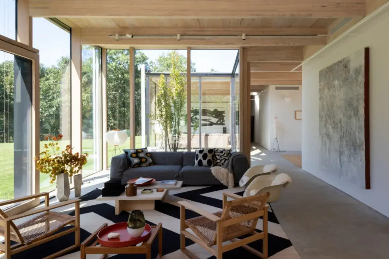 Ein heller Wohnraum mit viel Glas und Holz. Ein Sofa, zwei Sessel und ein Couchtisch laden zum Entspannen ein. Hier zeigt sich, wie werde ich minimalistisch: Weniger ist mehr.