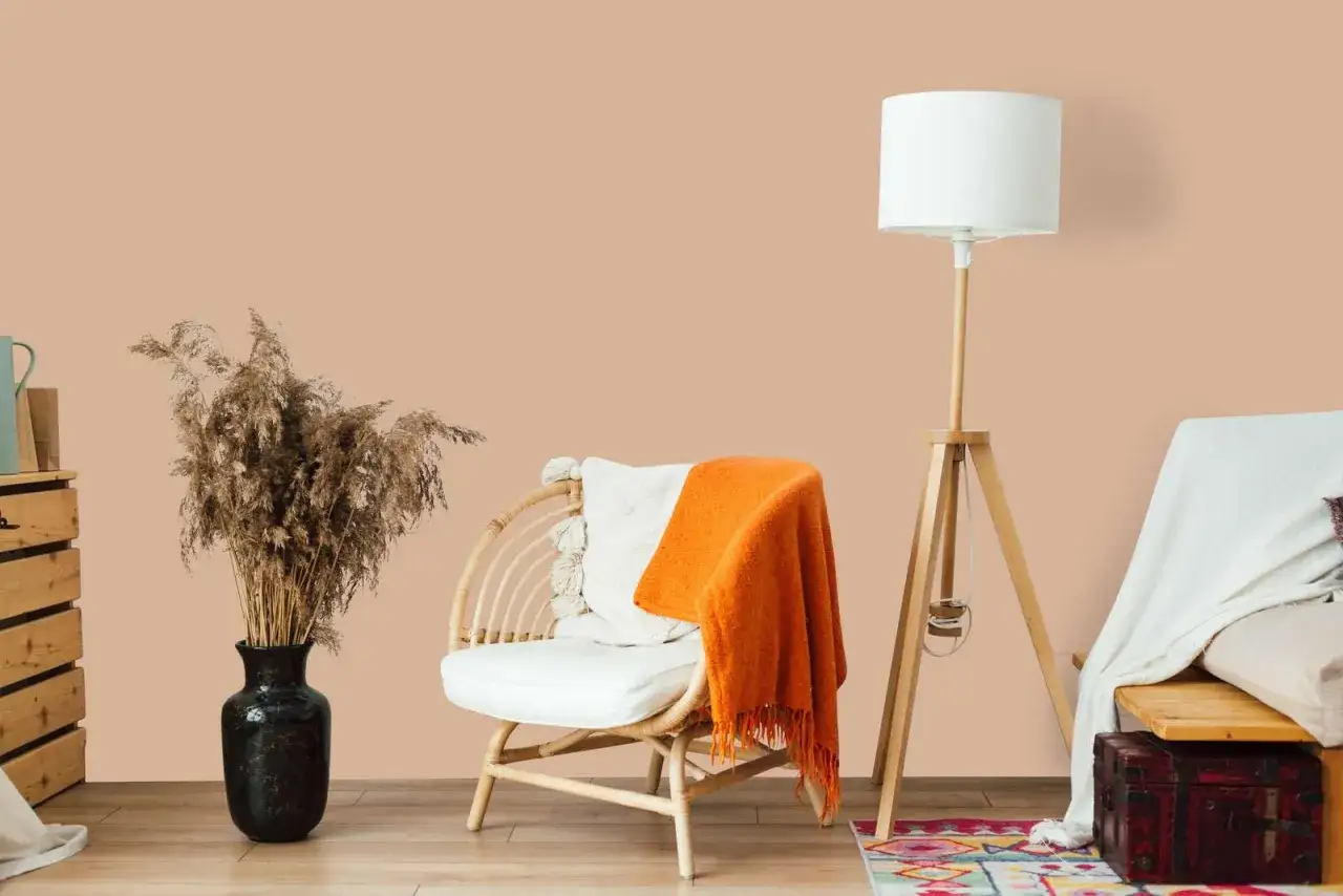 Gemütliche Ecke mit Rattan-Sessel, orangefarbener Decke und einem Strauß Pampasgras. Die Wand in warmem Pfirsichton ist eine der beliebten Wandfarben für ein einladendes Ambiente.
