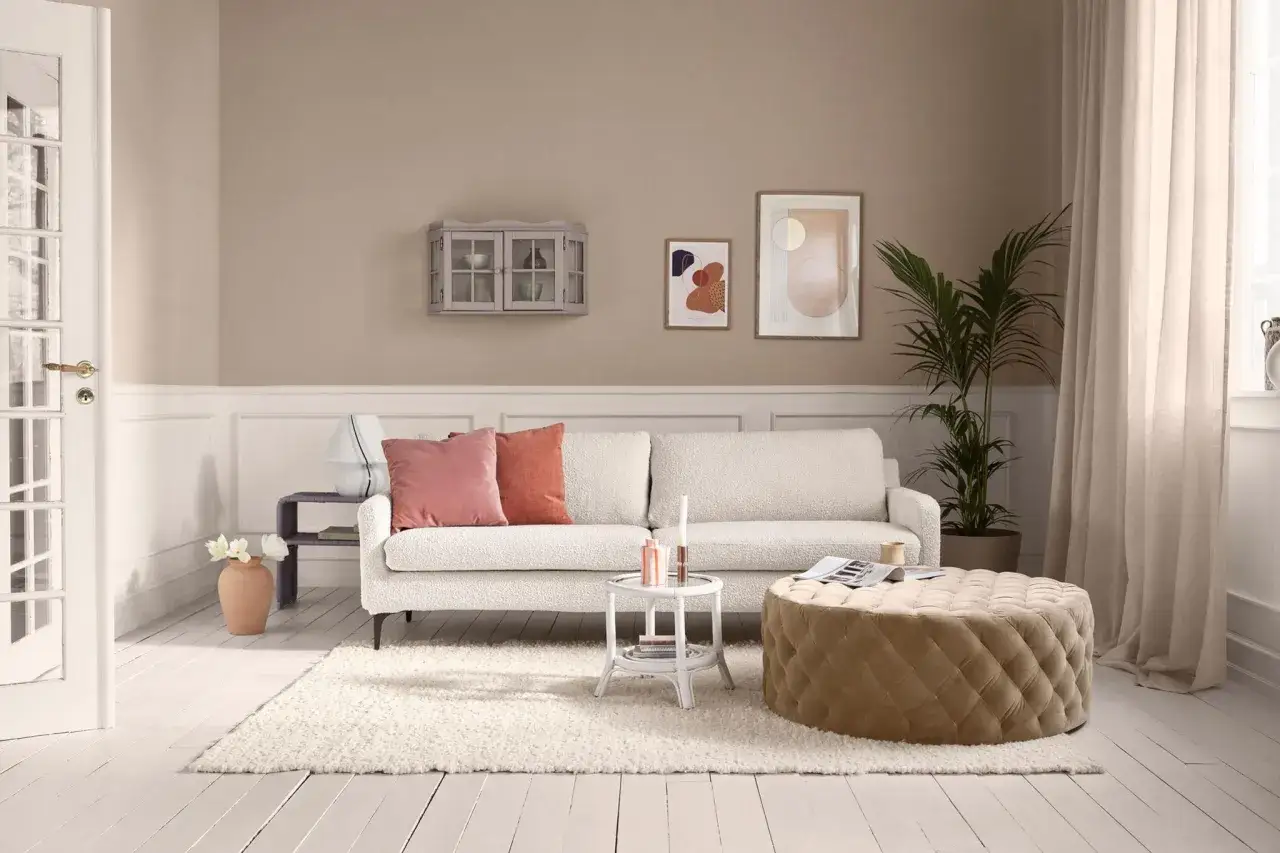 Gem&uuml;tliches Wohnzimmer mit beiger Wirkung: wei&szlig;es Sofa, Stepphocker, Teppich und Wandfarbe schaffen eine warme Atmosph&auml;re.