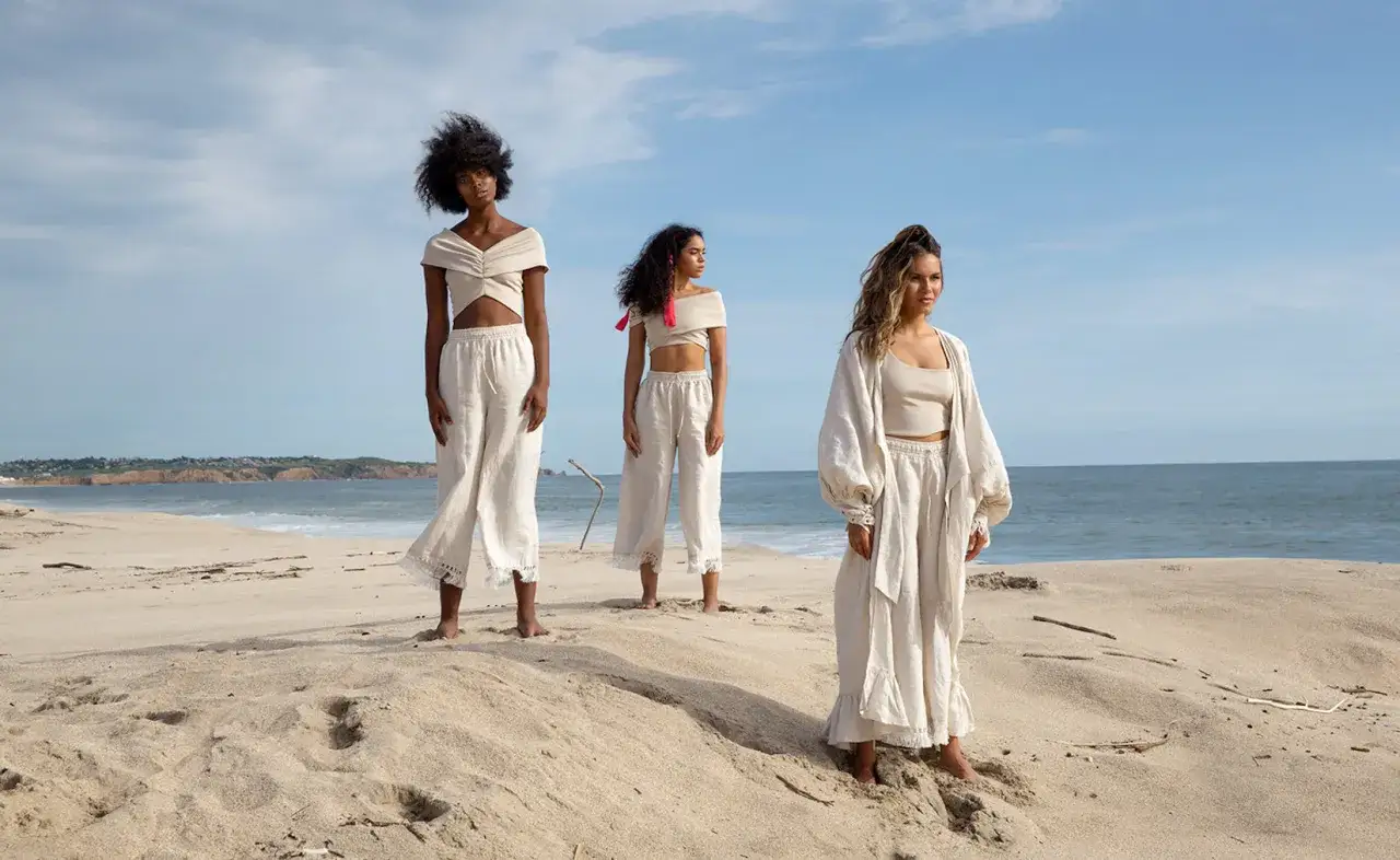 Drei Frauen in Leinenkleidung am Strand. Die Kleidung zeigt die slow fashion vorteile: zeitlos, nachhaltig und bequem.