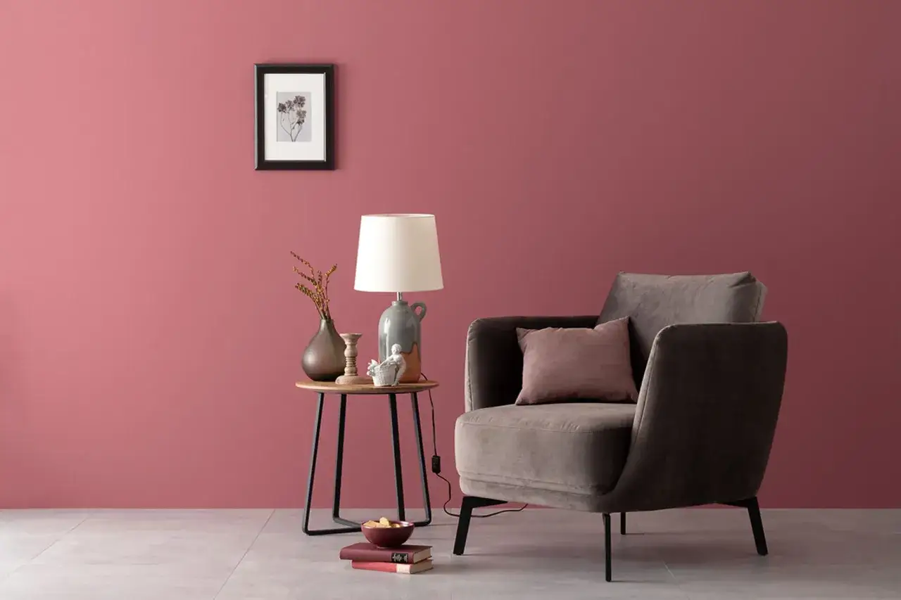 Gem&uuml;tliche Ecke mit Sessel und Beistelltisch vor einer Wand in einem warmen, englischen Rosenrot. Perfekt, um sich mit einem Buch zu entspannen.