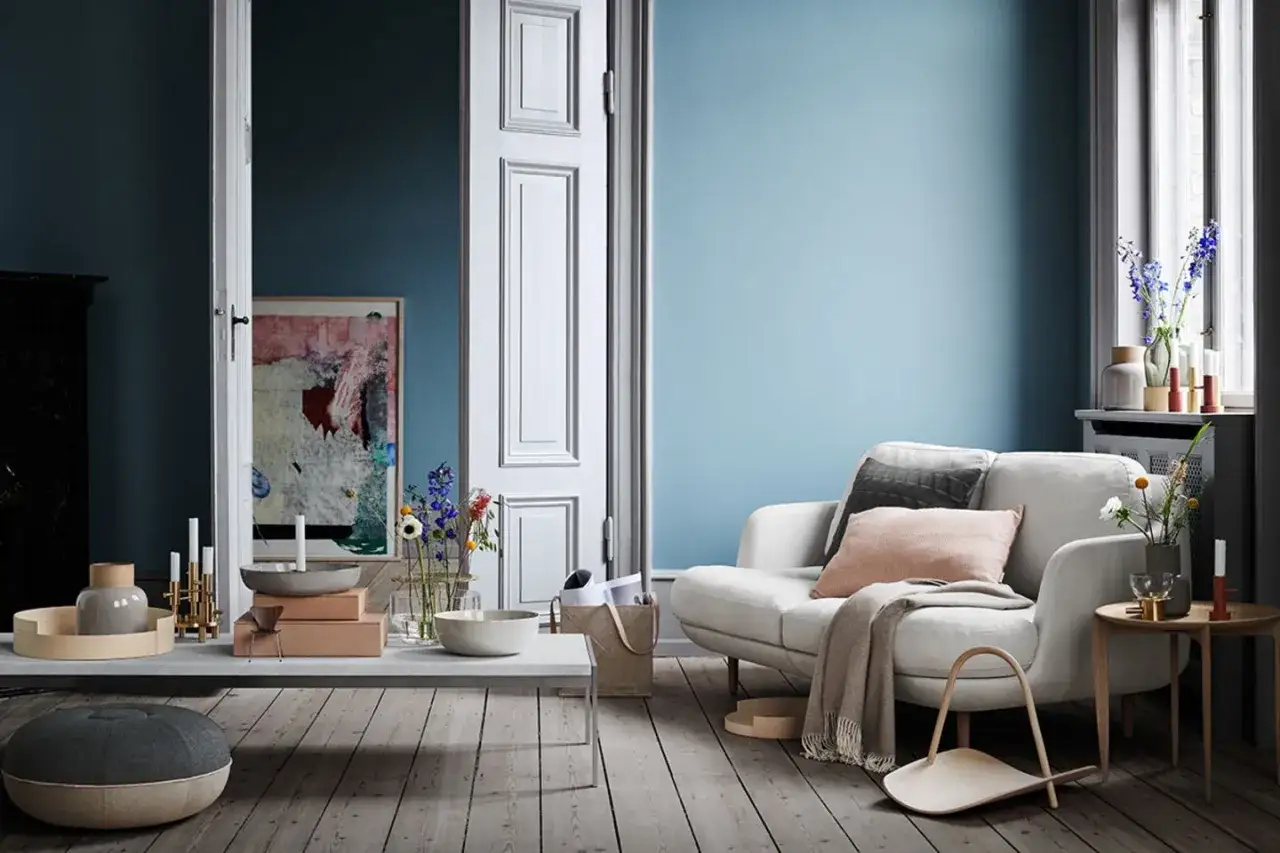 Ein gemütliches Wohnzimmer mit einer hellblauen Wand, einem weißen Sofa und einem abstrakten Gemälde.