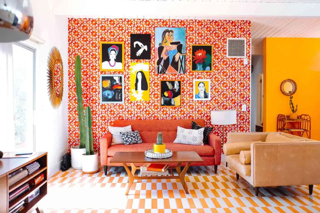 Lebendiges Wohnzimmer im 70er jahre einrichtungsstil mit orange gemusterter Tapete, bunten Bildern und einem Kaktus.