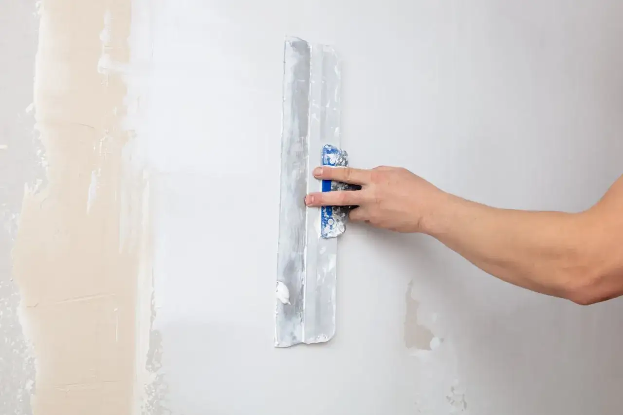 Hand gl&auml;ttet mit einem Spachtel eine Wand, um sie f&uuml;r das Tapezieren auf Putz vorzubereiten.