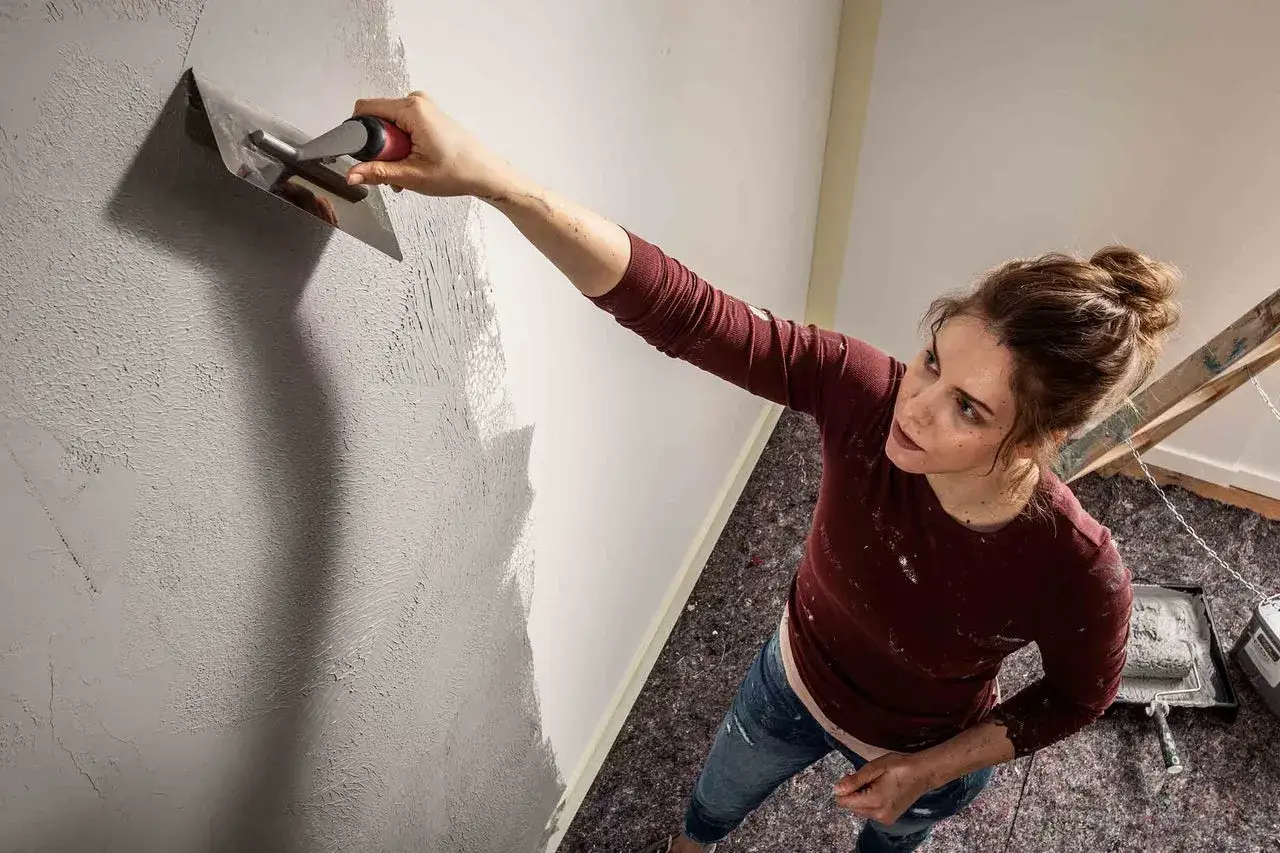 Frau gestaltet eine struktur wand mit einer Kelle.