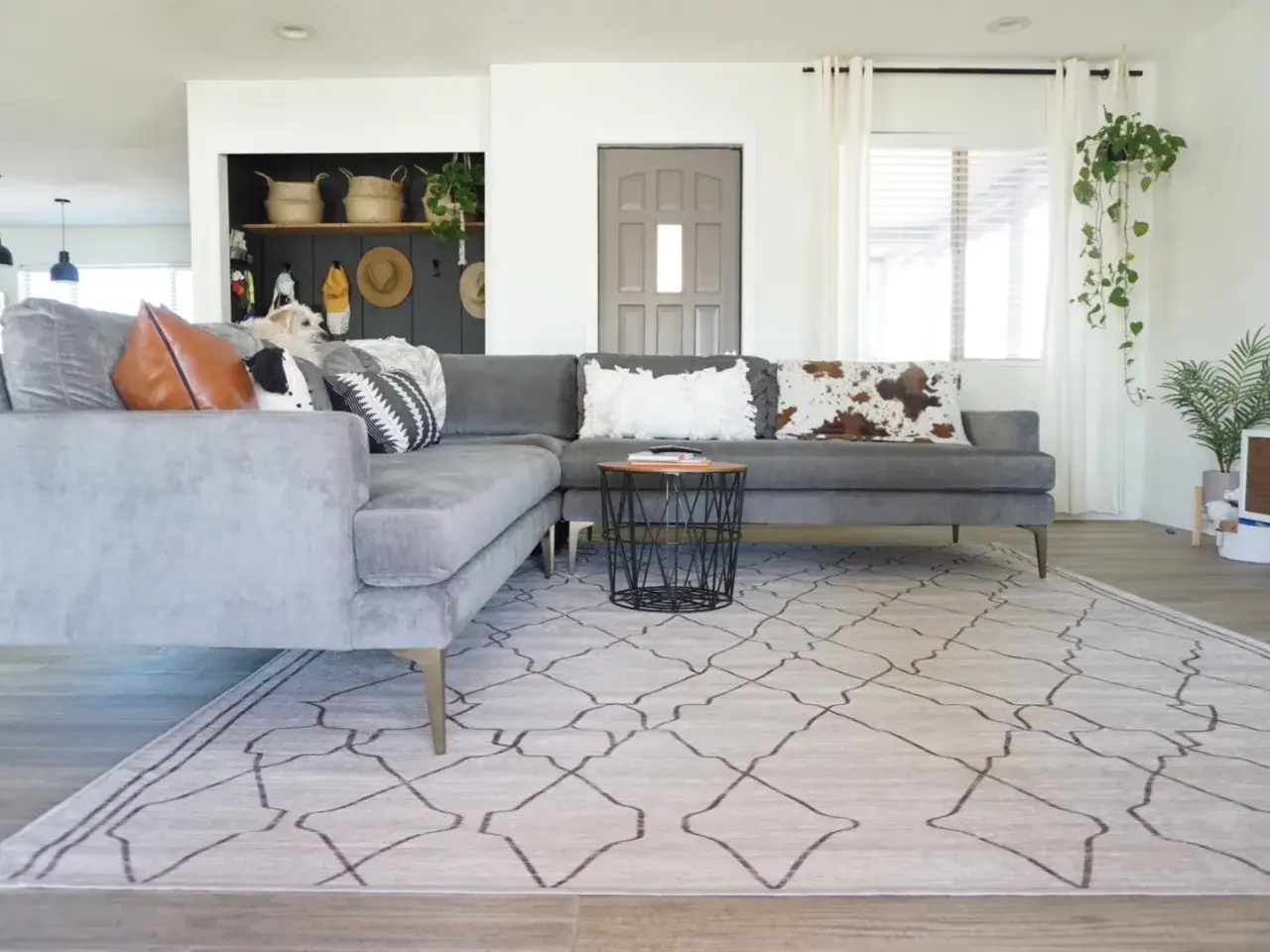 Graue Couch mit vielen Kissen, darunter ein Kuhfell-Muster. Ein Teppich mit geometrischem Muster liegt davor.