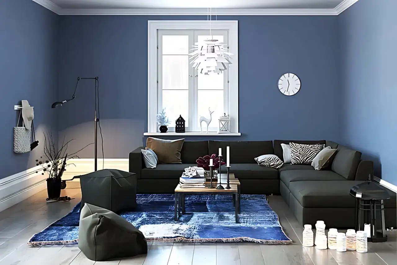 Gemütliches Wohnzimmer mit dunklem Sofa, blauer Teppich und Kissen. Ein Hocker aus Vlies steht im Vordergrund.