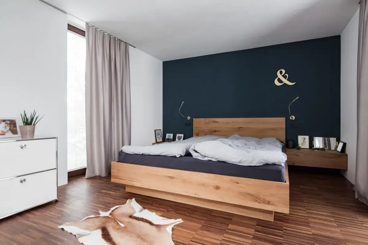 Modernes schlafzimmer blau holz: Ein Doppelbett aus hellem Holz steht vor einer dunkelblauen Wand. Daneben ein Nachttisch, ein weißer Schrank und ein Kuhfell-Teppich.