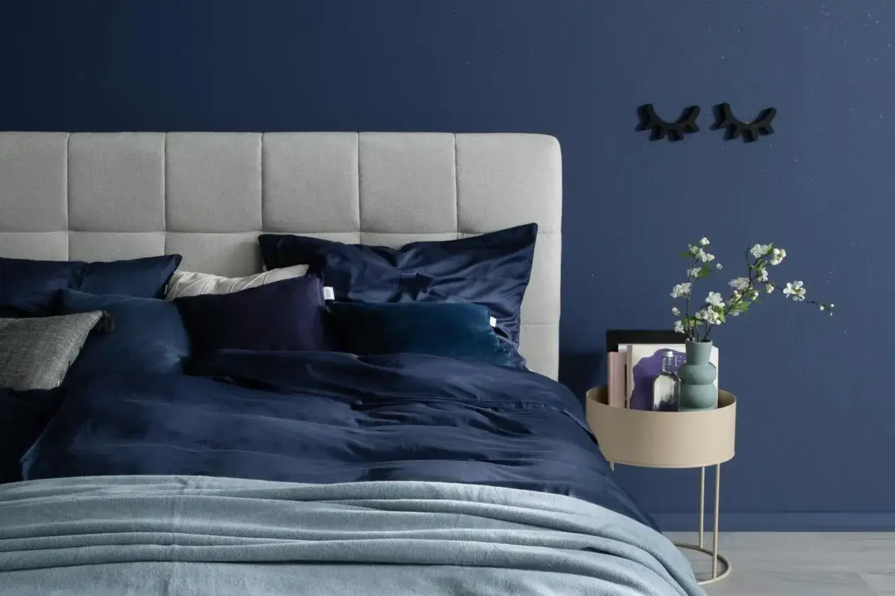 Ein gem&uuml;tliches Schlafzimmer, das man blau streichen m&ouml;chte. Dunkelblaue Bettw&auml;sche und ein hellgraues Kopfteil schaffen eine beruhigende Atmosph&auml;re.