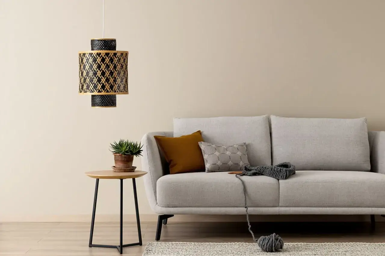 Gemütliches Wohnzimmer mit Sofa in beige grau farbe, einem Beistelltisch mit Pflanze und einer Hängelampe.