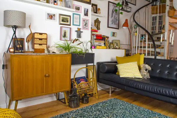 Gemütliche hygge einrichtung mit Vintage-Möbeln, Kunst und Pflanzen. Ein schwarzes Ledersofa lädt zum Entspannen ein.