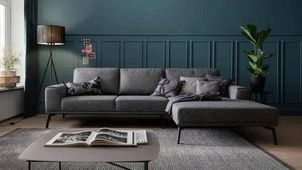 Gemütliche graue Couch mit vielen Kissen auf einem gemusterten Teppich. Ein moderner Couchtisch mit Buch steht davor.
