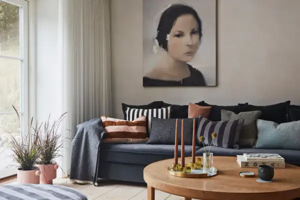 Gemütliches, warmes Wohnzimmer mit einem Sofa voller Kissen, einem Gemälde und einem Holztisch mit Kerzen.