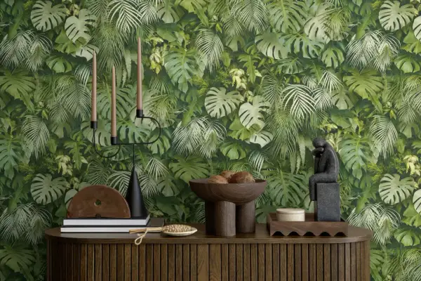 Dschungel-Tapete mit Monstera und Farnen. Ein Kerzenständer, Bücher und eine Skulptur stehen auf einem Holzmöbel. Der Unterschied Vlies und Papiertapete wird hier nicht gezeigt.