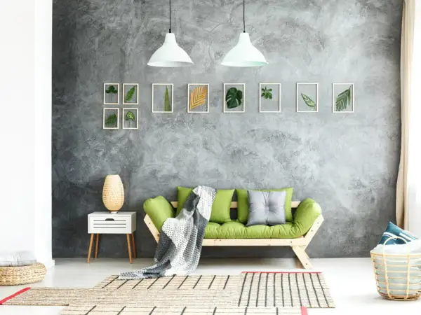 Graue Beton-Struktur Wand mit gerahmten Blättern und einem grünen Sofa.