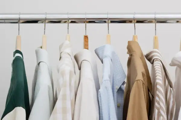 Eine Auswahl an Hemden und einem grünen Pullover für einen stilvollen **capsule wardrobe mann**.