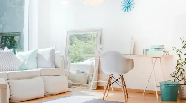 Ein helles, aufgeräumtes Wohnzimmer mit weißem Sofa, Spiegel und Schreibtisch. Perfekt, um das **Zimmer auszumisten** und Ordnung zu schaffen.