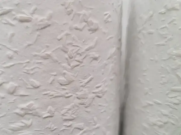 Nahaufnahme einer weißen Wand mit Raufaserputz innen. Die Struktur ist unregelmäßig und rustikal, perfekt für ein gemütliches Zuhause.