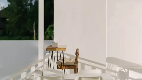 Ein Holztisch mit einer Box, ein Stuhl mit Kissen und weiße Möbel auf einer Terrasse. Hier lässt es sich schlicht und einfach leben.